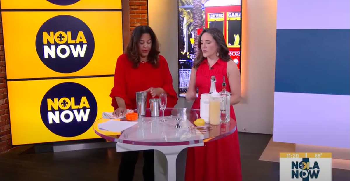 Camille Whitworth of New Orleans Drink Lab demonstrates a cocktail recipe on NOLA Now with a host, standing at a table with shakers, glasses, and ingredients.